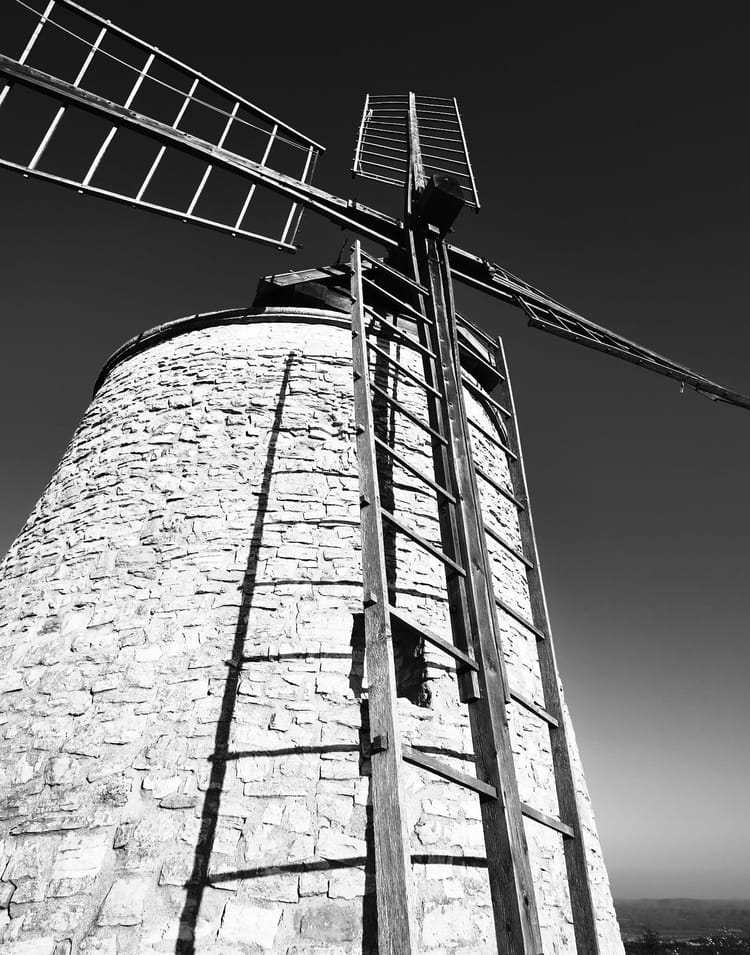 Schwarz-Weiß-Aufnahme einer alten steinernen Windmühle von unten, dramatisch gegen dunklen Himmel.